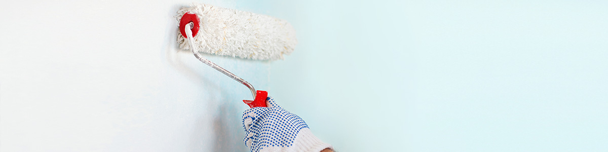 A hand with a dotted blue glove rolling a paint roller with light blue color paint for interior & exterior painting services in Calgary